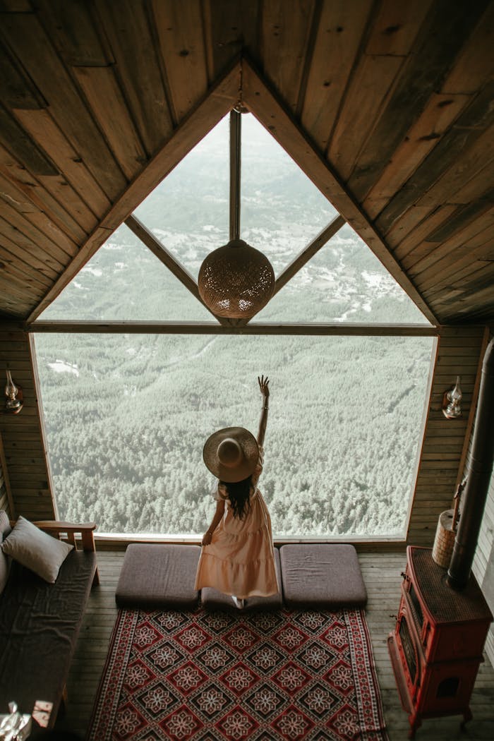 Woman in a rustic cabin enjoying view of Aladağ forest from large window.